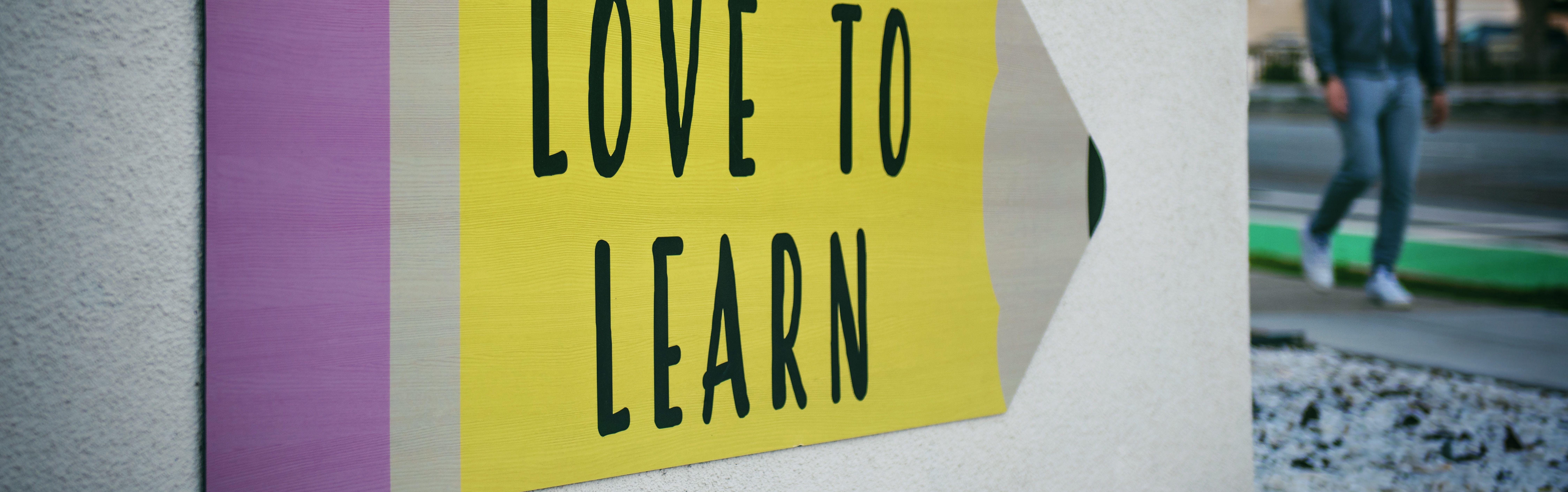 Ein Pfeil mit der Aufschrift "Wir lieben Lernen". Link zu den aktuellen Corona-Regeln