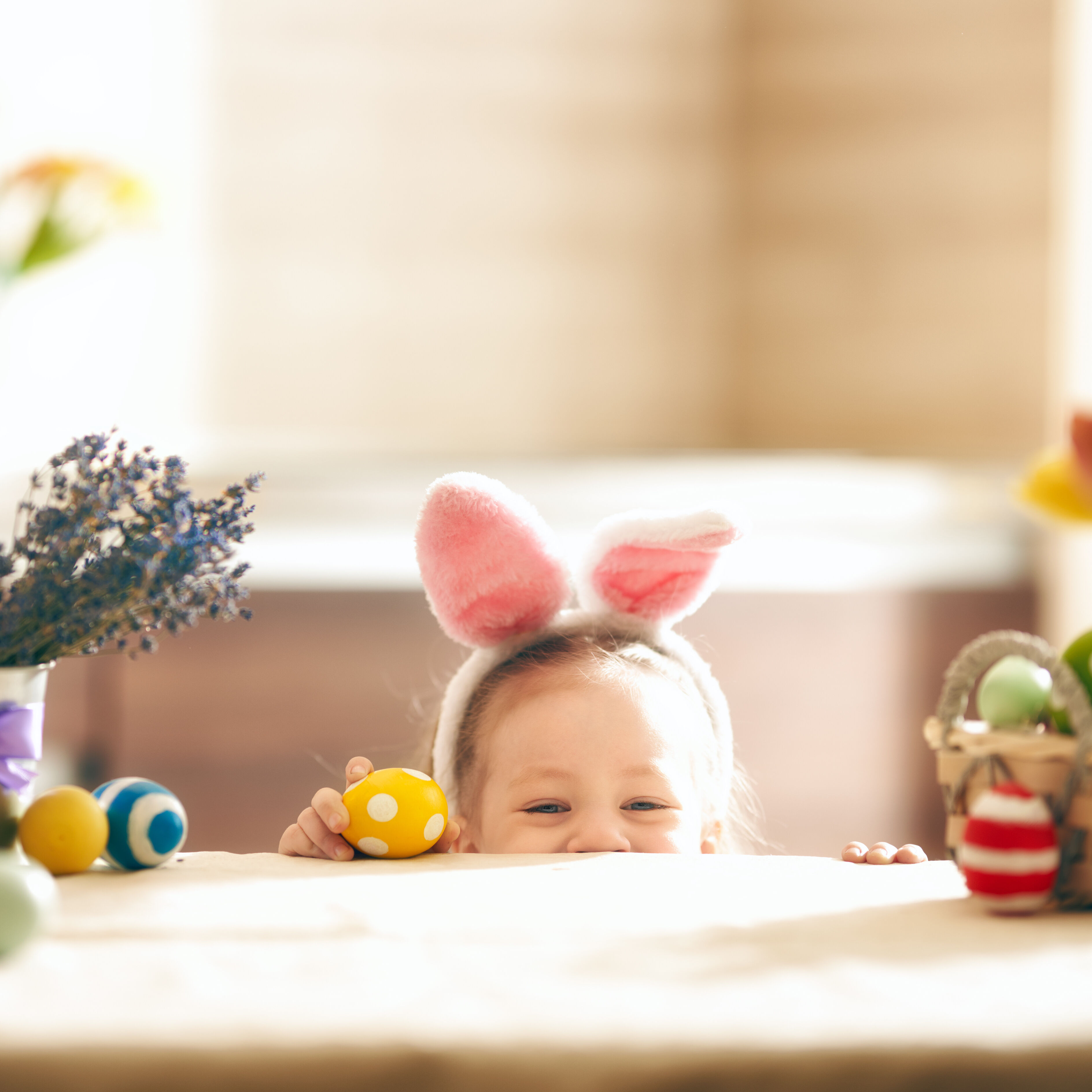 Kind mit Osterhasenohren versteckt sich halb unter dem Tisch.