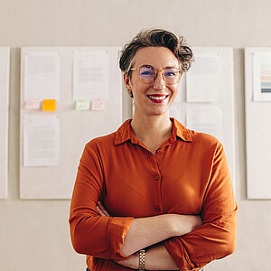 Eine Frau, mit verschränkten Armen, die vor einer Tafel steht.