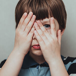 Kind hält sich die Augen zu und schaut hinter einem Finger hervor.