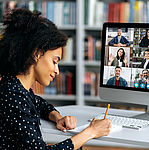 Frau sitzt am Schreibtisch und führt eine Videokonferenz mit einer Gruppe Menschen.
