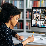Frau sitzt am Schreibtisch und führt eine Videokonferenz mit einer Gruppe Menschen. Link zu Online-Angeboten der VHS Unterland.