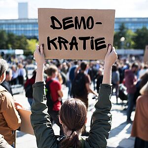 Frau mit einem Schild in der Hand, auf dem das Wort "Demokratie" steht.