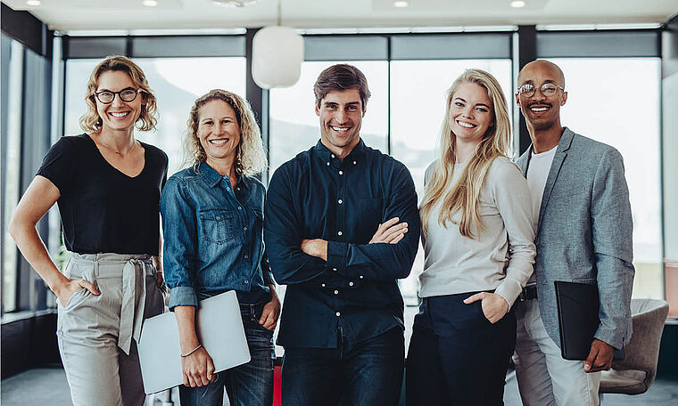 Eine Gruppe bestehend aus Männern und Frauen stehen im Büro.