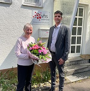 Eine ältere Frau hält einen Blumenstrauß in der Hand. Daneben steht ein Mann.