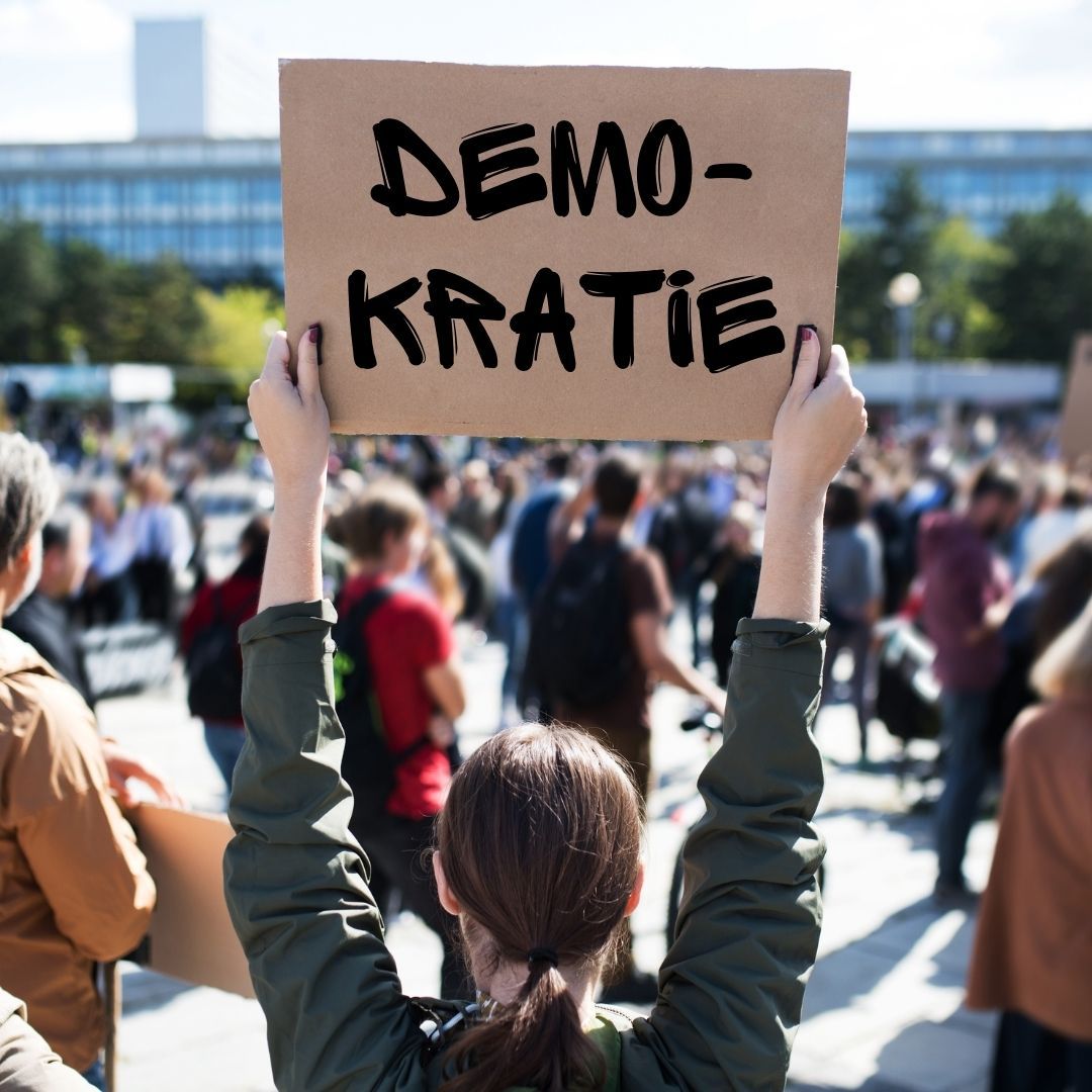 Frau mit einem Schild in der Hand, auf dem das Wort "Demokratie" steht.